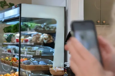 Hand mit Smartphone vor einer Kühltheke mit frischen Lebensmitteln
